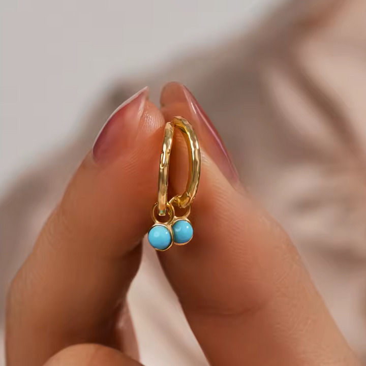 Gold earring with turquoise beads held between fingers on a light background