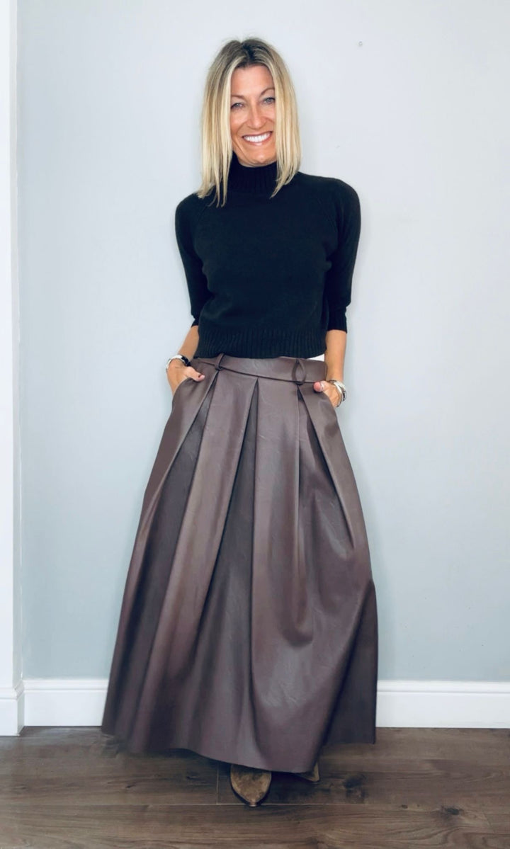 Woman wearing a black turtleneck and brown pleated skirt against a light blue wall.