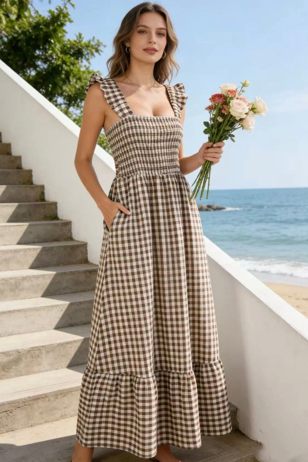 Woman in a checkered dress holding flowers on a staircase with ocean view