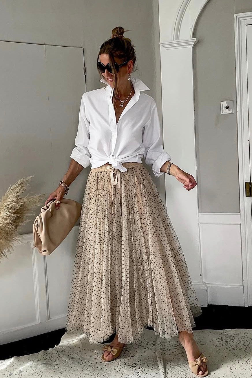 Woman in a white shirt and beige patterned skirt standing in a room with decorative elements.