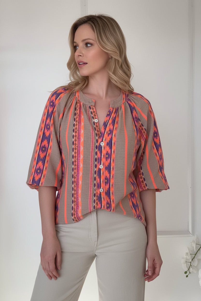 Woman wearing a colorful patterned blouse and beige pants against a white background