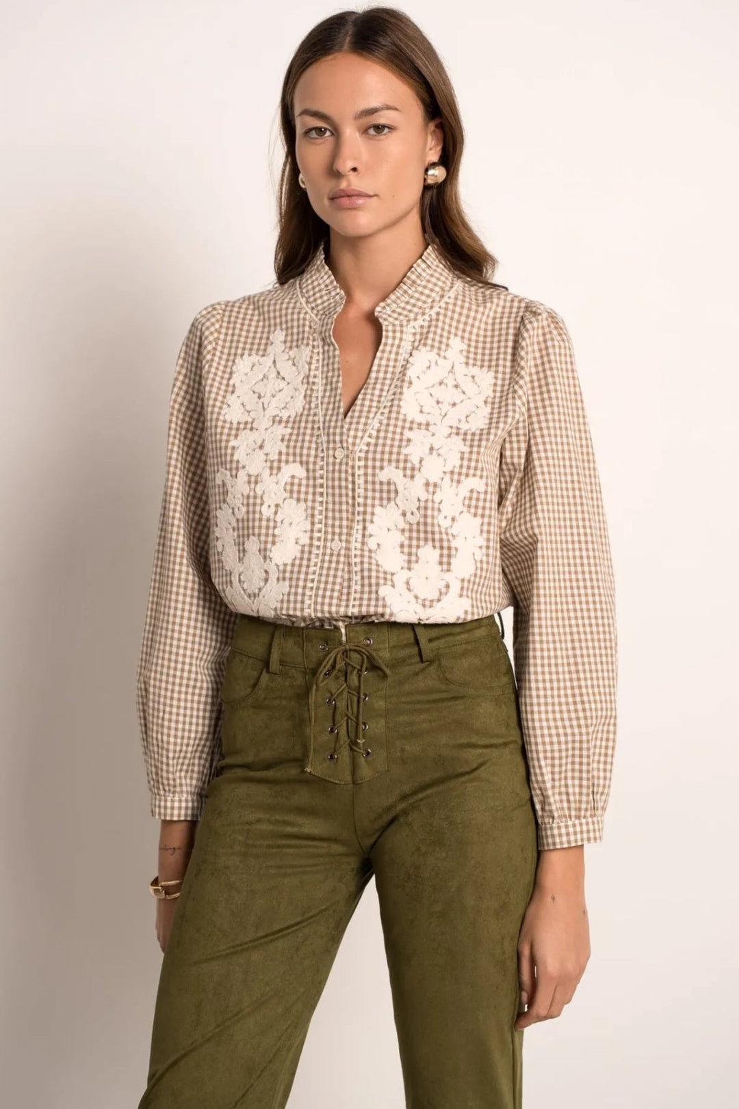 Woman wearing a checkered shirt with lace details and green pants on a plain background
