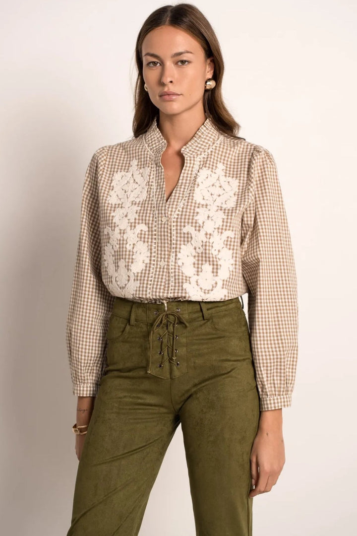 Woman wearing a checkered shirt with lace details and green pants on a plain background