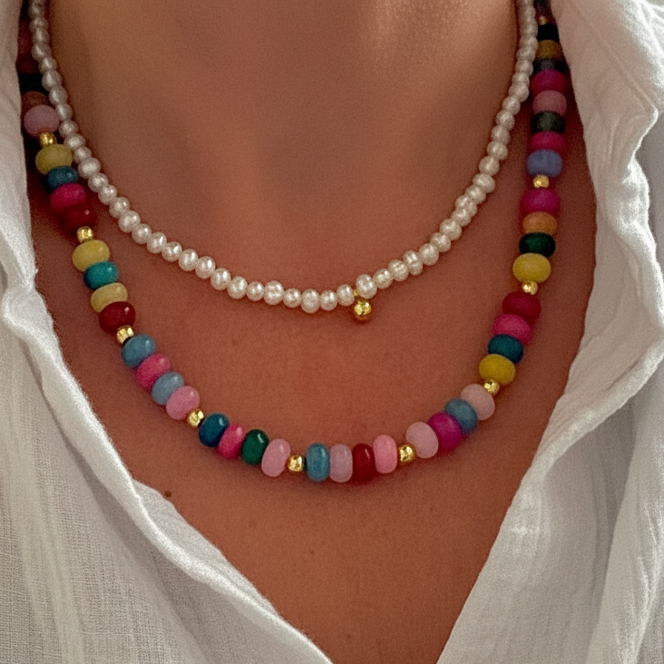 Colorful beaded necklace layered with a pearl necklace on a person wearing a white shirt.