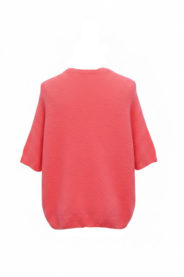 A coral pink knit short-sleeve top displayed on a mannequin from the back, wearing a cream bouclé bucket hat with a black band. The mannequin is set against a white wall decorated with colorful butterfly stickers.