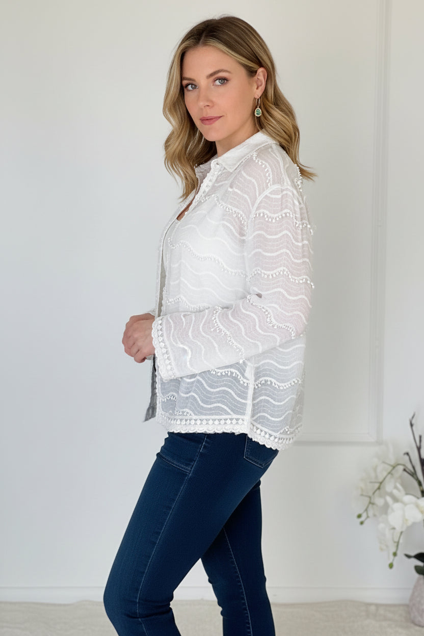 Person wearing a white lace top and blue jeans against a plain background