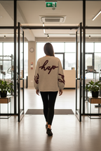 Person wearing a white sweatshirt with red text, standing in a minimalistic room with a plant.