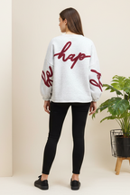 Person wearing a white sweatshirt with red text, standing in a minimalistic room with a plant.