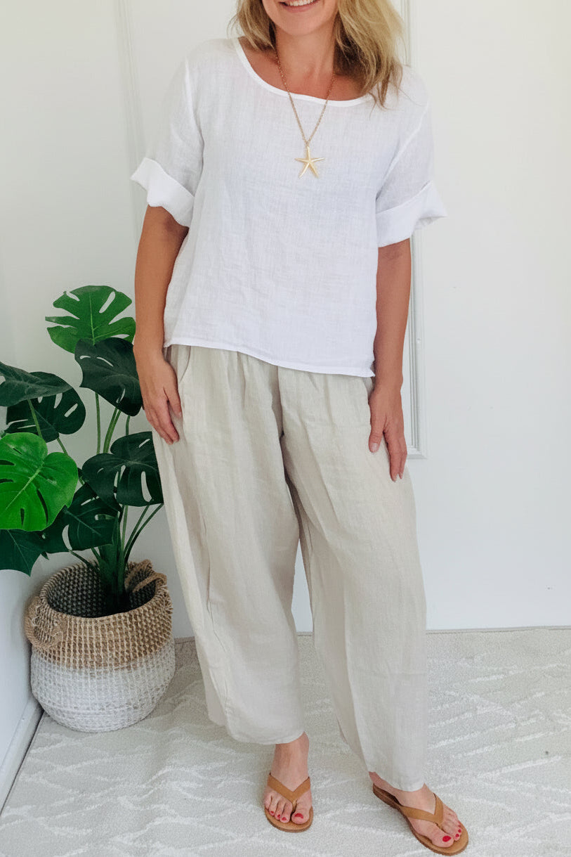 Woman wearing a white top and beige pants standing in a room with a plant.