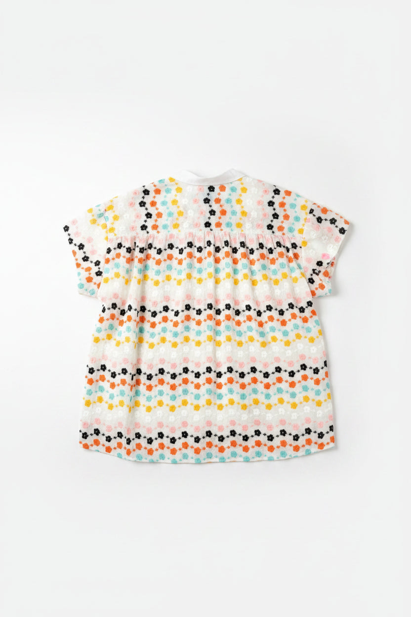 Short-sleeve shirt with colorful floral pattern on a hanger against a wooden door.