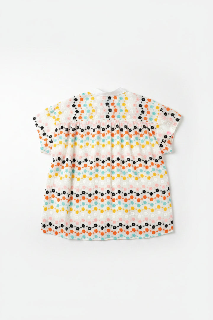 Short-sleeve shirt with colorful floral pattern on a hanger against a wooden door.