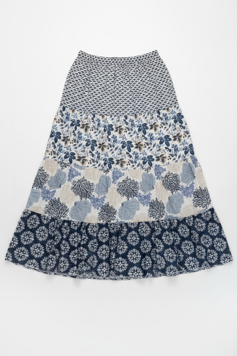 A tiered A-line skirt with a multi-patterned design, featuring a black and white geometric print on the top, a blue and white floral pattern in the middle, and a navy blue and white floral ruffle at the bottom, displayed flat against a white background.