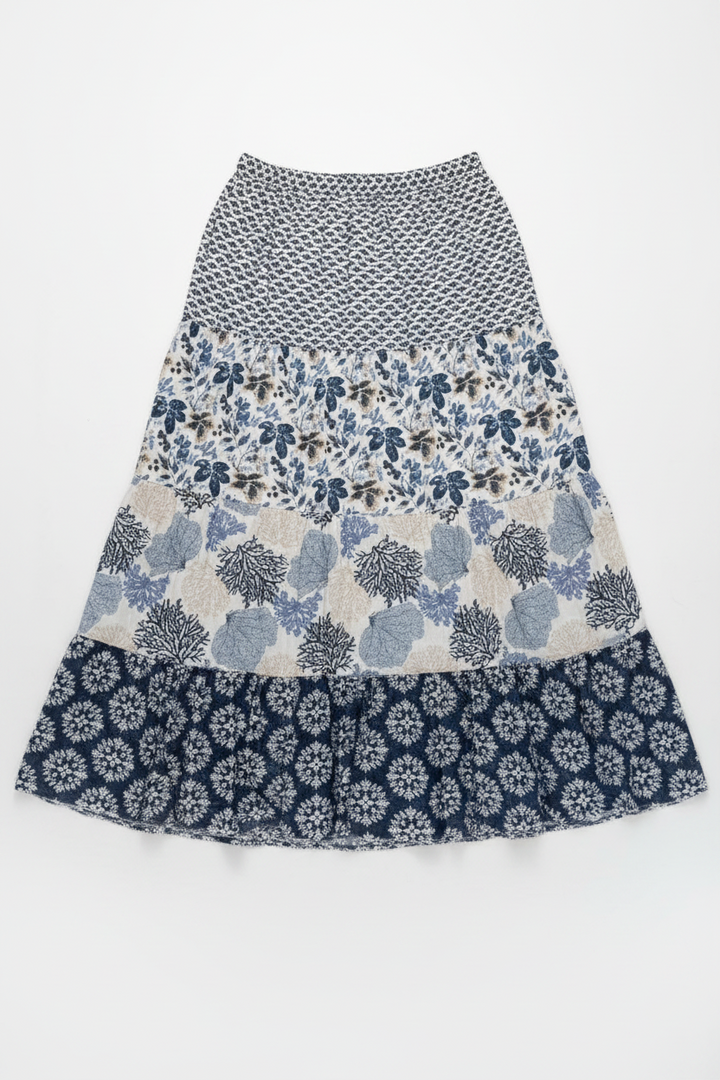 A tiered A-line skirt with a multi-patterned design, featuring a black and white geometric print on the top, a blue and white floral pattern in the middle, and a navy blue and white floral ruffle at the bottom, displayed flat against a white background.