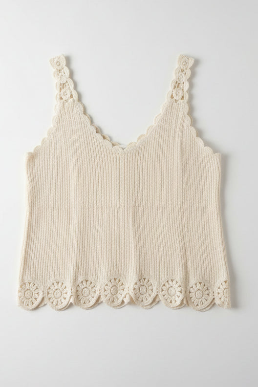 An off-white textured knit garment with scalloped and lace trim, hanging on a black rack in a cluttered indoor setting.