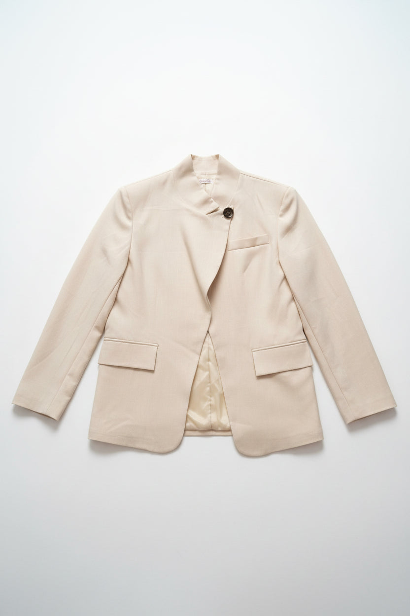 A light beige wrap-style blazer with a single dark button closure, displayed on a hanger on a clothing rack inside a retail store.