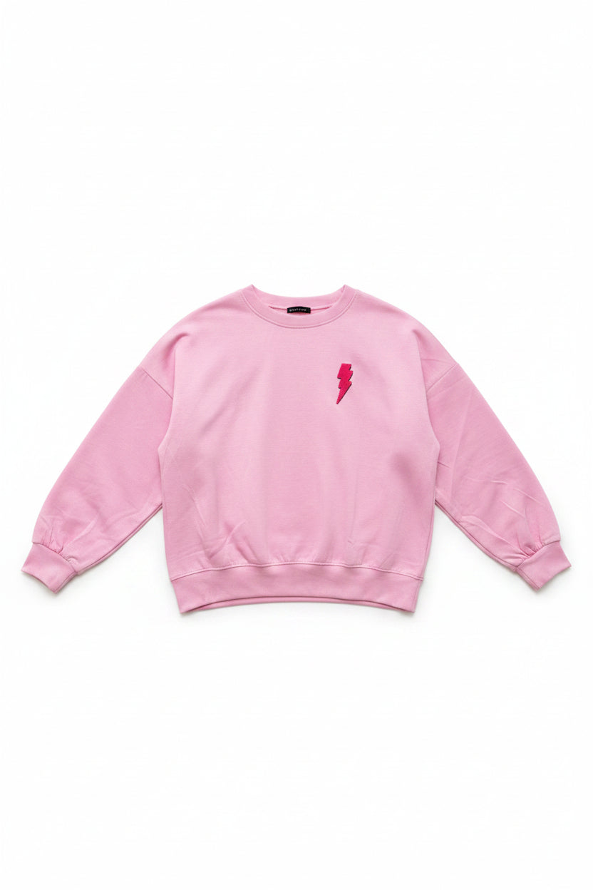A light pink crewneck sweatshirt with a small red lightning bolt graphic on the left chest, displayed on a white hanger on a wheeled dolly in an indoor setting.