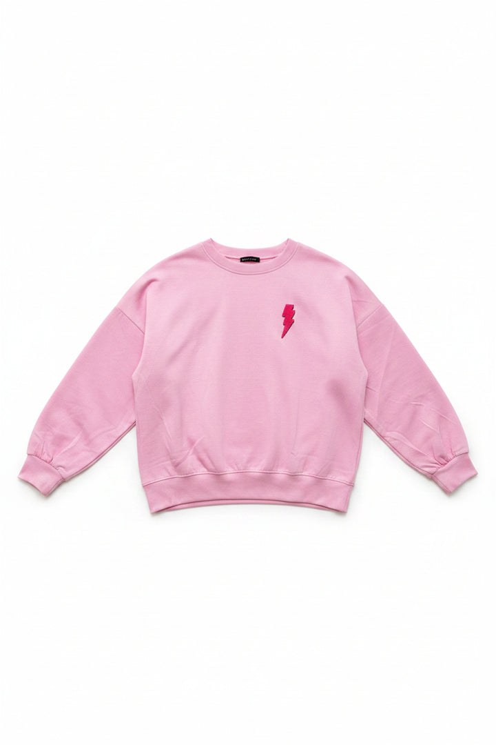 A light pink crewneck sweatshirt with a small red lightning bolt graphic on the left chest, displayed on a white hanger on a wheeled dolly in an indoor setting.