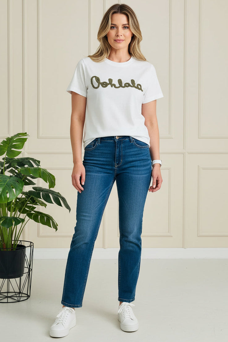 Woman wearing a white t-shirt with 'Ooh La La' text and blue jeans, standing indoors.