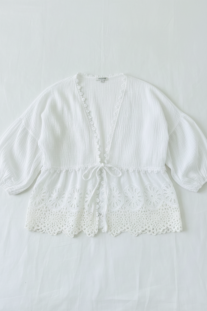 Person wearing a white lace-trimmed cardigan over a red top and blue jeans.