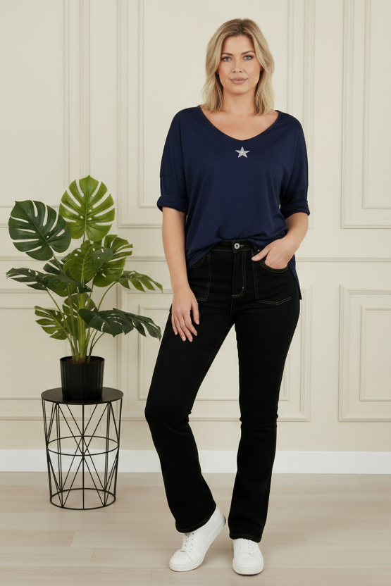 Woman in navy top and black jeans standing next to a plant in a room with paneled walls.
