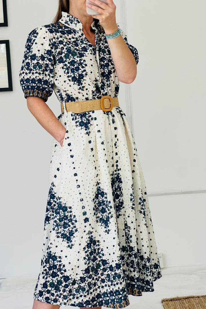 Woman wearing a floral dress with a belt against a white wall