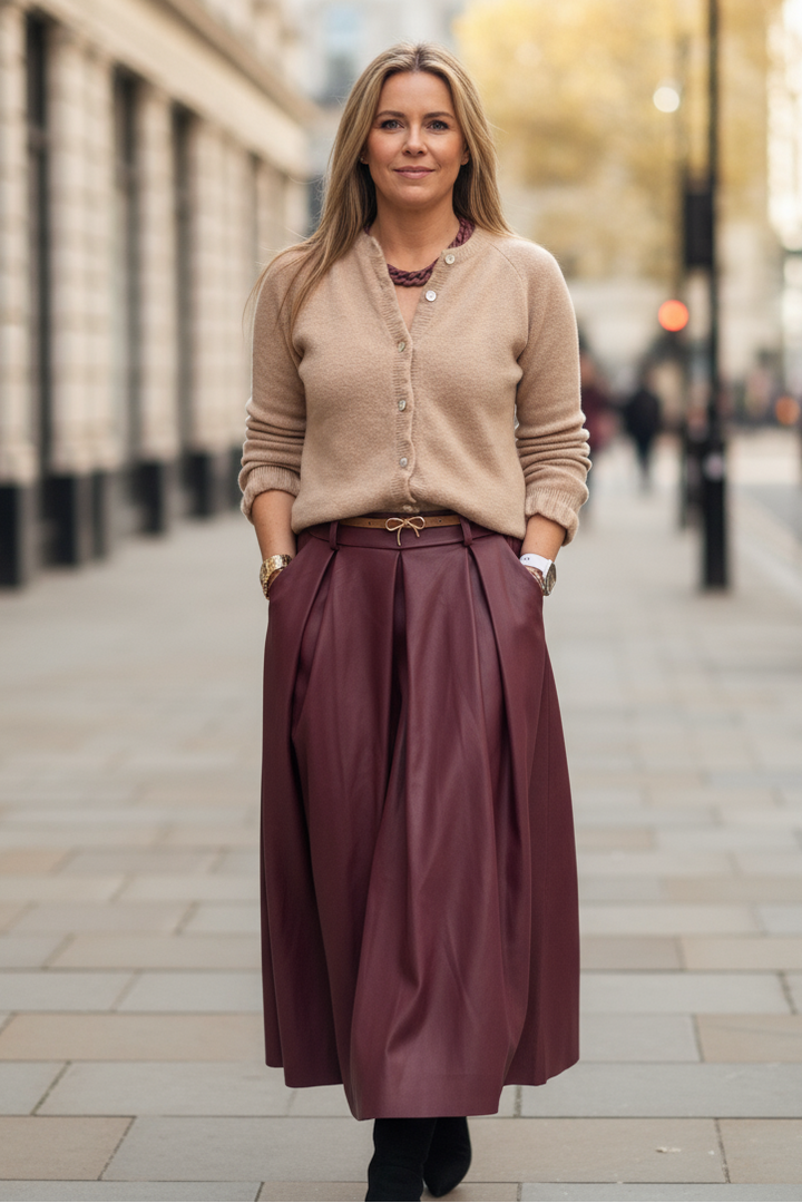 Woman in a beige cardigan and burgundy skirt standing on a city street.