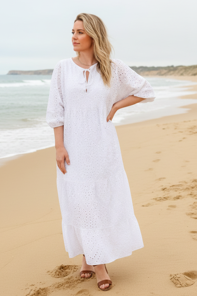 Woman in a white dress standing on a beach with ocean in the background