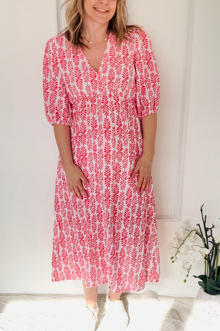 Woman wearing a red and white patterned dress standing against a white wall.