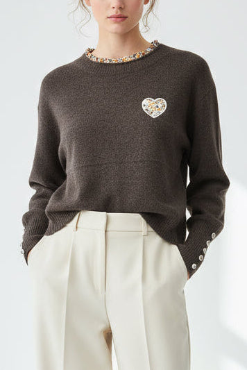 Person wearing a dark brown sweater with a heart design and white pants on a light gray background