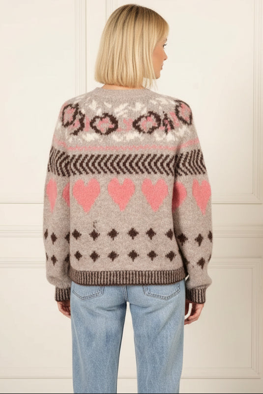 Person wearing a patterned sweater with hearts and geometric designs in a room setting.