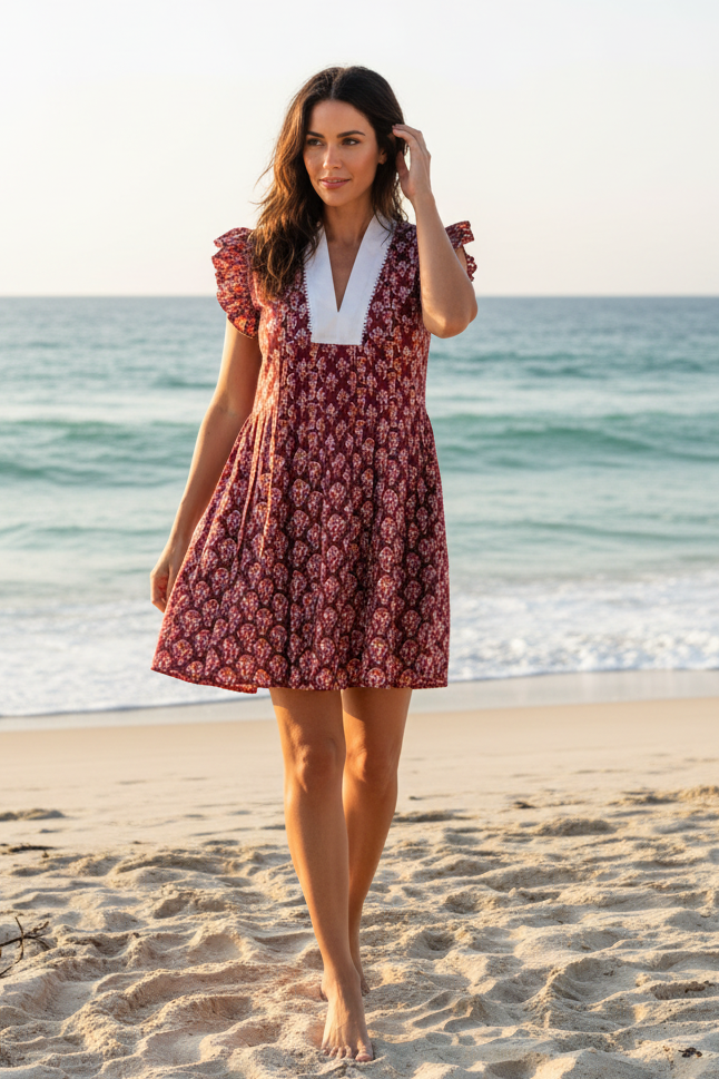 Woman in a red floral dress standing on a beach with ocean in the background