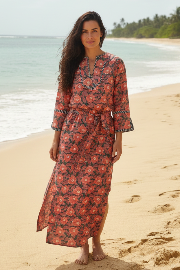 Woman in a floral dress standing on a beach with ocean and trees in the background