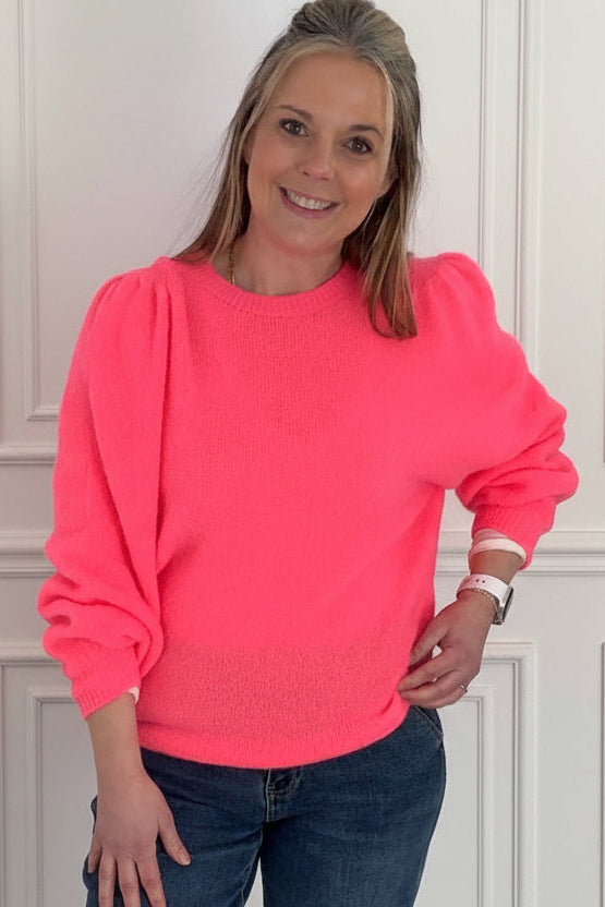 Woman wearing a bright pink sweater and blue jeans indoors.