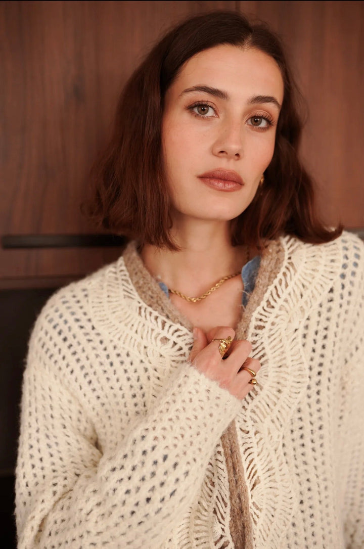 Woman wearing a beige knitted cardigan with a wooden background