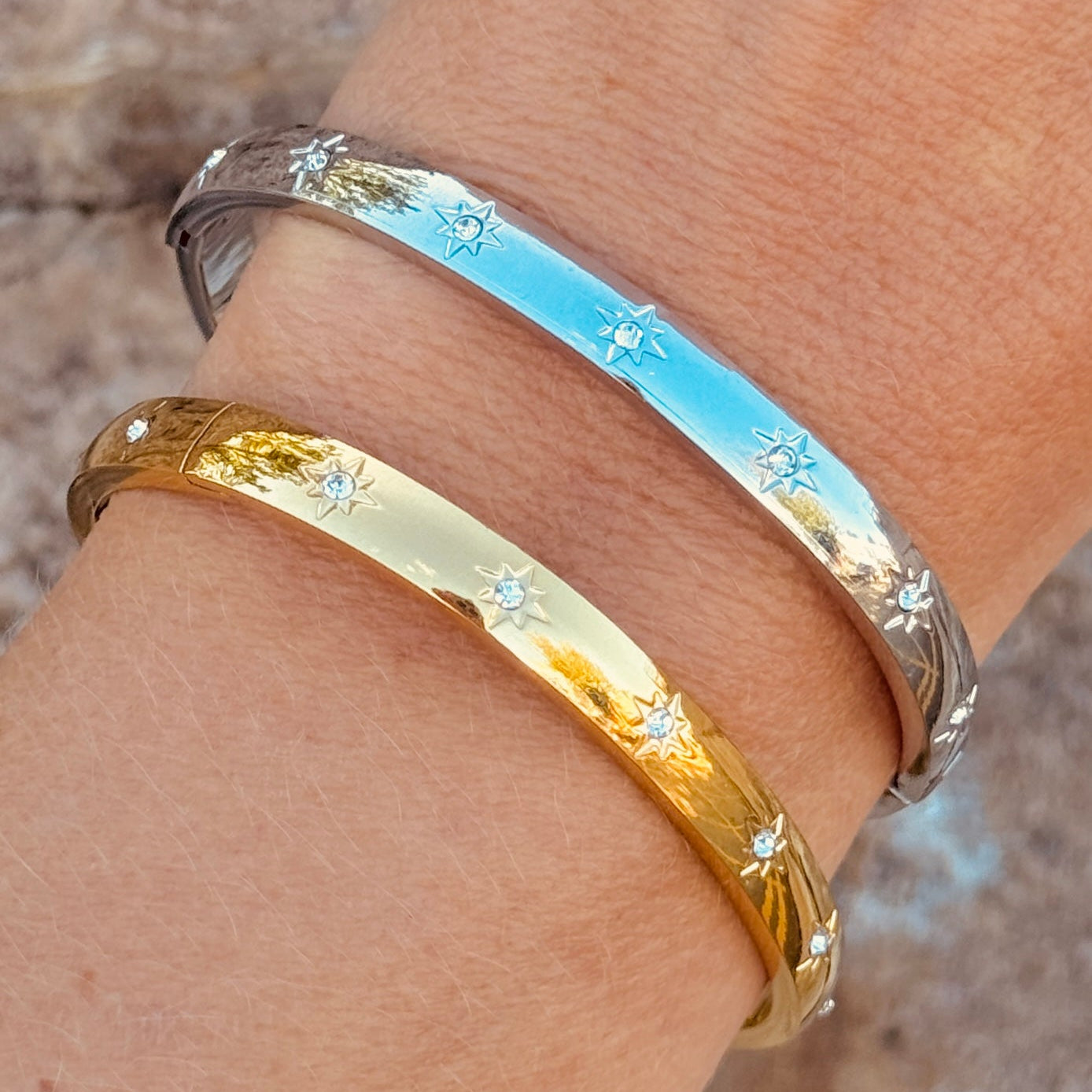 Two gold and silver bangles on a wrist with a blurred natural background