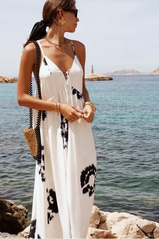 Woman in a white dress with black patterns standing by the ocean.