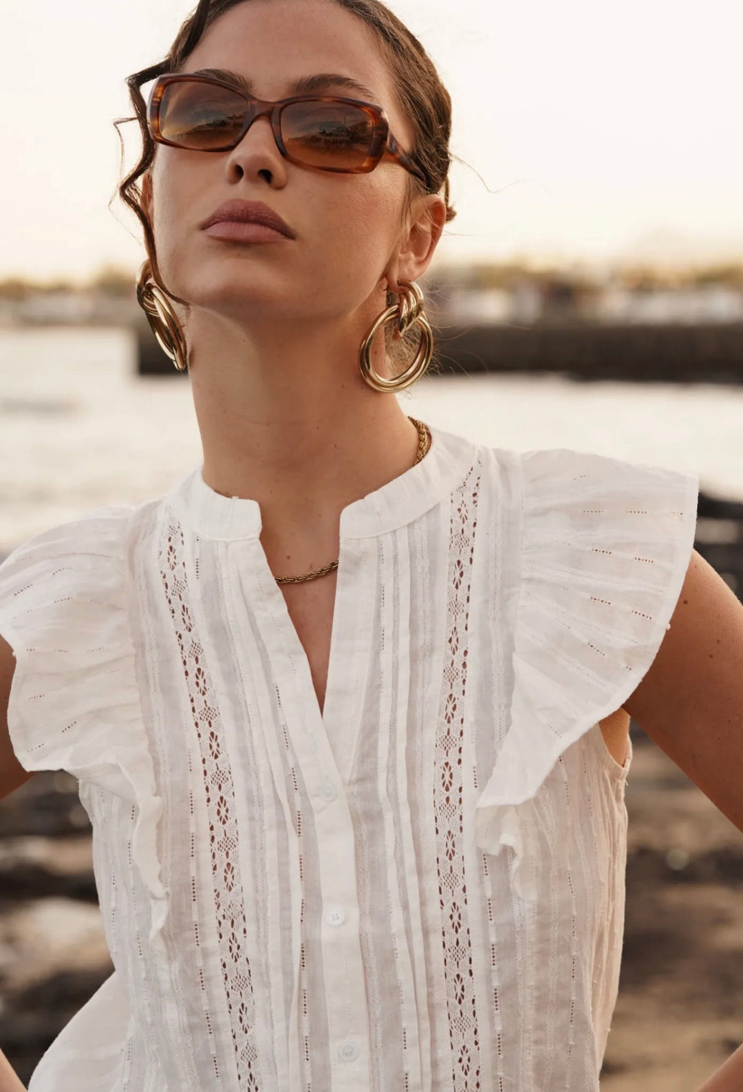 Woman wearing a white blouse with ruffled sleeves by a waterfront.