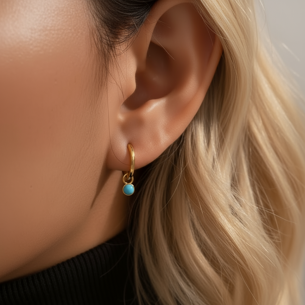 Close-up of an ear wearing a gold earring with a turquoise gemstone.