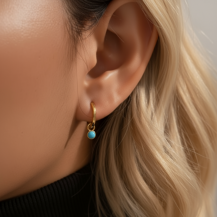 Close-up of an ear wearing a gold earring with a turquoise gemstone.