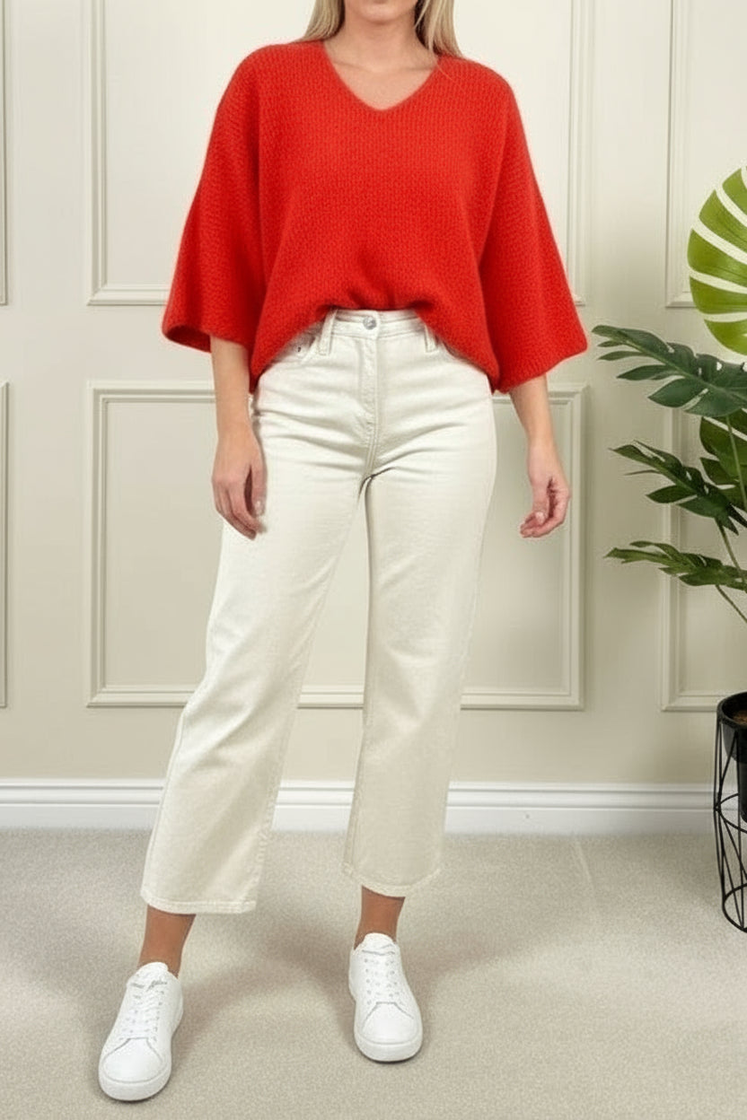Person wearing a red sweater and light blue jeans standing in front of a mirror.