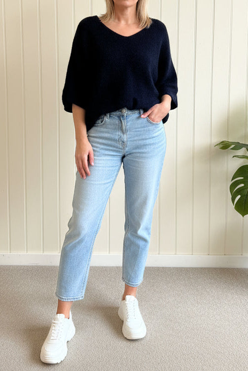 Person wearing a navy sweater, light blue jeans, and white sneakers in a minimal indoor setting.