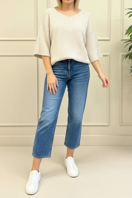 Person wearing a beige sweater and light blue jeans standing in front of a decorative mirror.