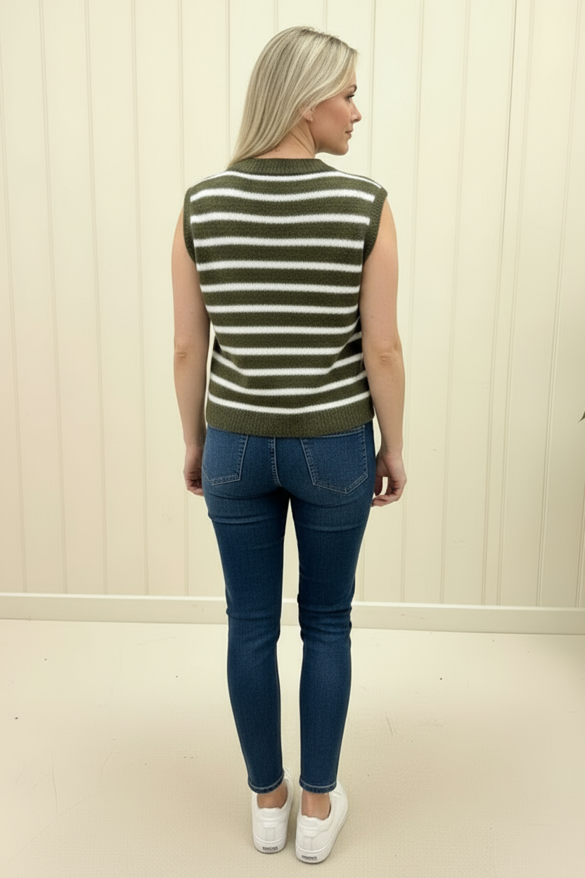 Woman wearing a green and white striped sweater and blue jeans against a beige wall.