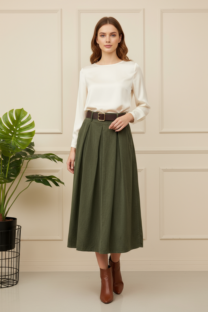 Woman wearing a white blouse and green skirt standing in a room with a plant.