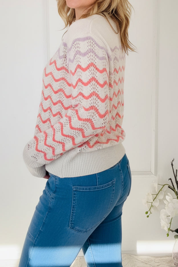 Woman wearing a patterned sweater standing in a room with a vase of flowers.