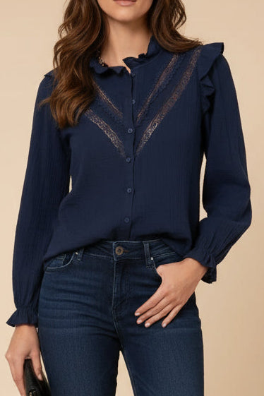 Woman wearing a navy blue blouse with lace details and dark jeans on a beige background