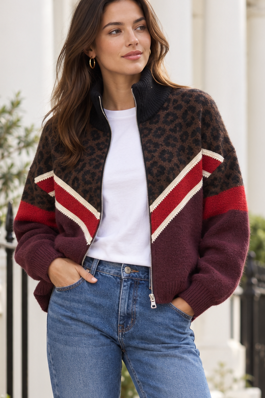 A woman wearing a fuzzy zip-front cardigan with a brown leopard print, burgundy, and red-and-cream striped panels, styled with a white T-shirt and blue jeans.