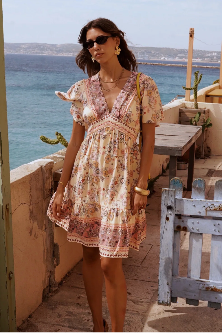 Woman in a patterned dress standing on a balcony with ocean view