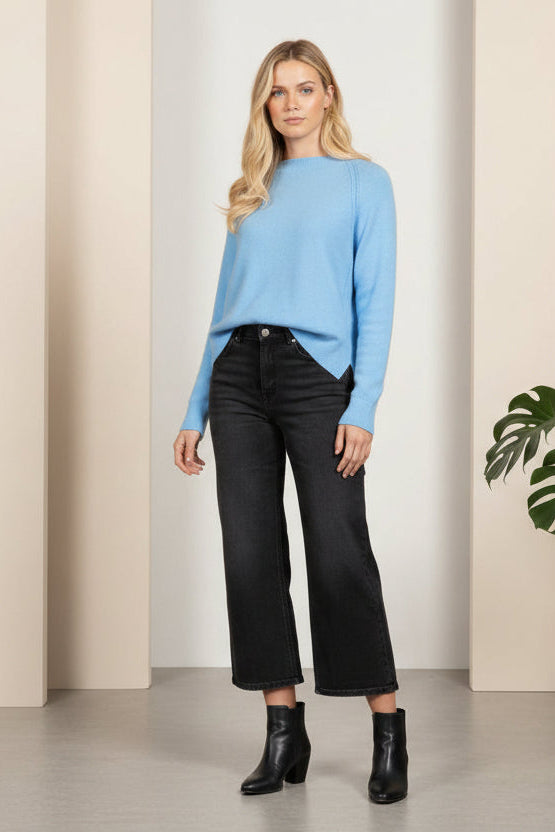 Person wearing a white sweater and dark jeans on a gray background