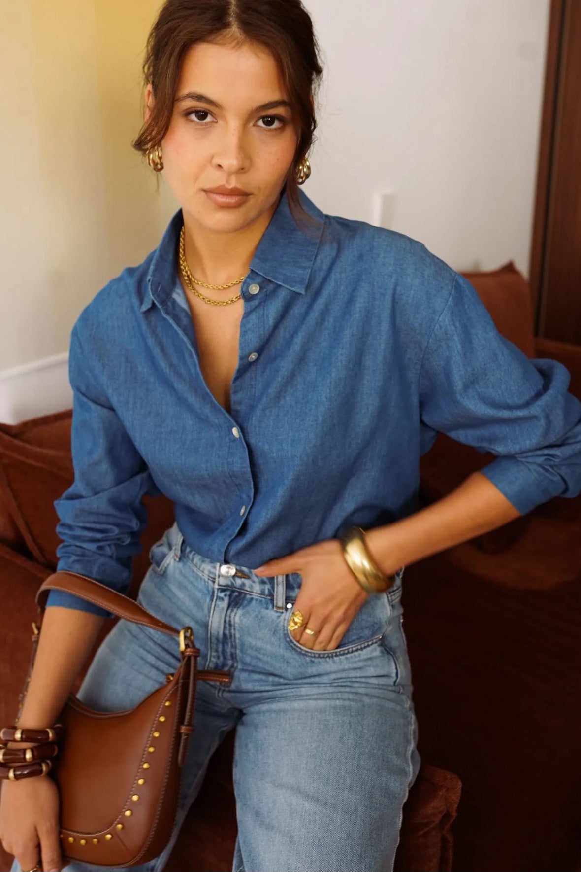Woman wearing a blue denim shirt and jeans, standing indoors.